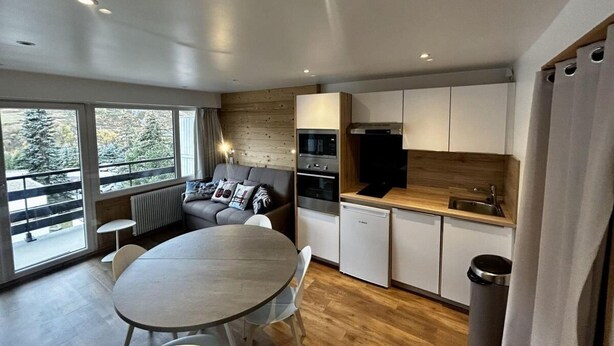 A compact kitchen with modern appliances, a dining area with a round table, and a sofa near large windows. - 10m from ski slopes, 2nd floor, view mountain, tv, ski locker, 27m², Les Menuires (Les Menuires)