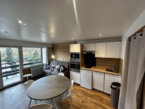 A compact kitchen with modern appliances, a dining area with a round table, and a sofa near large windows. - 10m from ski slopes, 2nd floor, view mountain, tv, ski locker, 27m², Les Menuires (Les Menuires)