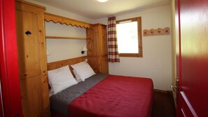 A bedroom with a bed, wooden headboard, a window with curtains, and a wall-mounted light fixture.
