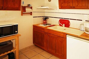 A compact kitchen with a microwave, sink, and red kettle.