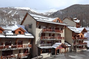 A multi-story hotel with balconies, ski slopes in the background, and a snowy landscape.