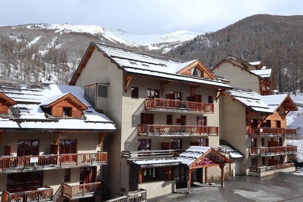A multi-story hotel with balconies, ski slopes in the background, and a snowy landscape.