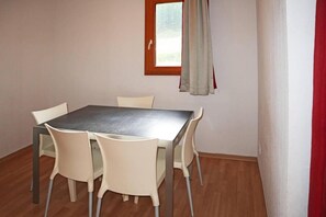 A dining area with a rectangular table and four chairs, a window with curtains, and a wooden floor.