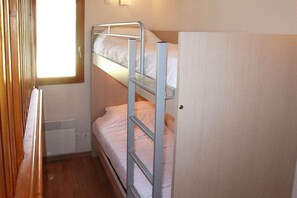 A bunk bed room with a wooden floor, a window, and a door.