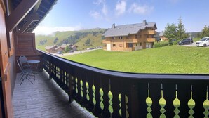 A wooden deck with a railing, a table with chairs, and a view of a house and cars in a green landscape. - 50m from ski slopes, 1st floor, view mountain, balcony, tv, ski locker, 29m², Les Saisies (Les Saisies)