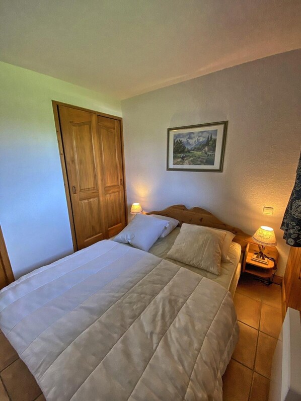 A bedroom with a large bed, two bedside tables with lamps, a wooden wardrobe, and a framed picture on the wall.