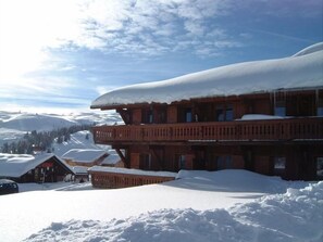 A wooden lodge with a snow-covered roof and multiple balconies, surrounded by a snowy landscape.