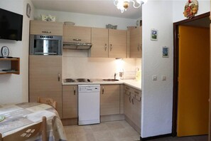 A compact kitchen with a dishwasher, stove, and microwave. There is a dining table with chairs and a small shelf with a clock. - Resort center, 2nd floor, balcony, tv, ski locker, 22m², Les Orres (Les Orres)