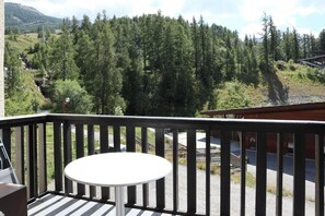 A balcony with a round table, overlooking a forested area with a mountain in the background.