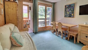 A cozy room with a wooden bed, a dining table with chairs, a TV, and a window with a view of greenery. - 10m from ski slopes, 4th floor, 27m², Méribel-Mottaret (Méribel - Les Allues)