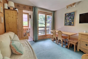 A cozy room with a wooden bed, a dining table with chairs, a TV, and a window with a view of greenery. - At the foot of shops, 4th floor, 27m², Méribel-Mottaret (Méribel - Les Allues)