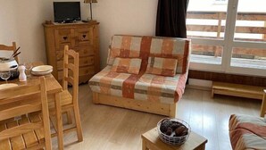 Ein gemütliches Wohnzimmer mit einer Holzsofa, einem Esstisch mit Stühlen, einer kleinen Holzkabine und einem Fernseher auf einem Schrank.