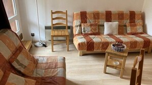 Ein gemütliches Wohnzimmer mit Holzboden, einer Couch, einem Sessel und einem kleinen Tisch mit einem Korb.