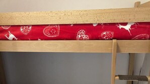 Ein Etagenbett mit einer roten, gemusterten Matratze und einer grauen, gemusterten Decke.
