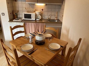 A dining area with a wooden table set for four, equipped with plates, cutlery, and a central pot. A microwave and coffee maker are visible in the background. - 200m from resort center, 4th floor, tv, 25m², Orcières Merlette 1850 (Orcières)