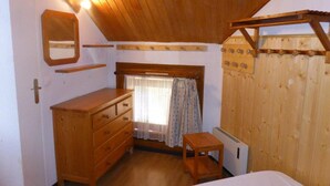 Un dormitorio con techo de madera, cómoda de madera, una mesita, una ventana con cortinas y un radiador.