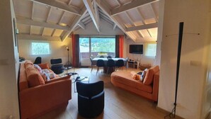 A spacious living room with high ceilings, a dining area, and a TV mounted on the wall. - 4th floor, view resort, fireplace or stove, parking, tv, ski locker, 160m², Serre Chevalier (La Salle-les-Alpes)