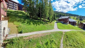 A hillside hotel with a stone entrance, a paved path leading to the buildings, and a forested backdrop. - 100m from ski slopes, 4th floor, balcony, ski locker, 37m², Montchavin La Plagne (Bellentre)