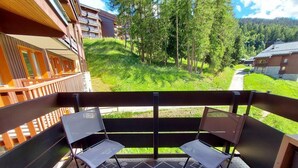 A balcony with two chairs and a table, overlooking a green hillside with trees and buildings. - 100m from ski slopes, 4th floor, balcony, ski locker, 37m², Montchavin La Plagne (Bellentre)