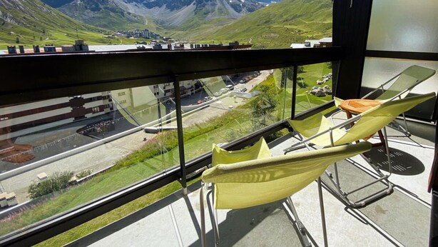A balcony with a yellow hammock chair, a view of a mountainous landscape, and a road with buildings in the distance. - 10m from ski slopes, 4th floor, balcony, tv, ski locker, 52m², Tignes (Tignes)