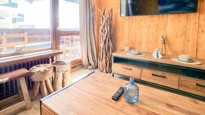 Ein Holzinnenraum mit an der Wand montiertem Fernseher, einem Holztisch mit einer Flasche und einem Fenster mit Vorhängen.
