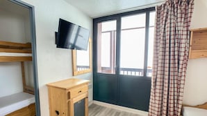 A room with bunk beds, a wooden cabinet, a television, and a large window with curtains. - 100m from resort center, 4th floor, balcony, tv, ski locker, 30m², Tignes (Tignes)