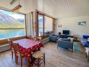 Uma sala de estar acolhedora com área de jantar, grandes janelas com vista para as montanhas, uma televisão e uma lareira.