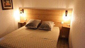 A single bed with a polka dot bedspread and two pillows, flanked by wooden nightstands with wall-mounted lamps.