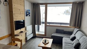 A cozy living room with a sofa, a TV, a wooden table, and a window with curtains.