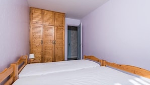 A bedroom with a wooden wardrobe, a bed with white bedding, and a nightstand with a lamp.