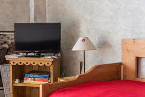 Une pièce avec un lit, un téléviseur posé sur un meuble en bois, une lampe et quelques livres.
