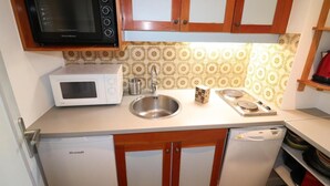 A compact kitchen with a microwave, a white oven, a sink, and a small stove.