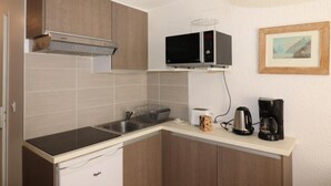 Une cuisine compacte équipée d’un micro-ondes, d’un grille-pain et d’une machine à café sur le plan de travail, d’un évier et d’armoires en bois.