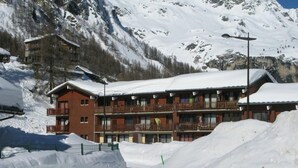 Un hôtel à plusieurs étages, doté de balcons, entouré de neige et de montagnes.