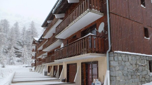 Un bâtiment en bois à plusieurs étages, doté de balcons, de murs en pierre et surplombant un paysage enneigé.