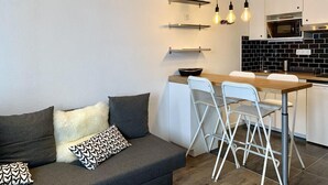 Moderni keittiö, jossa on valkoiset kaapit, mustat laatat välitilassa sekä ruokailutila, jossa on valkoinen pöytä ja tuolit.