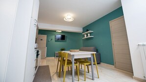 En kompakt opholdsstue med spiseplads, med et hvidt bord og gule stole, en grå sofa og en væg i turkis.