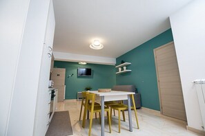 Un ambiente compatto con zona pranzo, un tavolo bianco e sedie gialle, un divano grigio e una parete verde acqua.