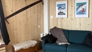 A cozy room with wooden walls, a teal sofa, a fur-covered bench, and framed pictures on the wall. - 100m from ski slopes, 2nd floor, balcony, tv, 25m², Tignes (Tignes)