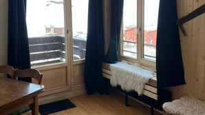 A room with a wooden floor, a dining table, a bench with a fur throw, and a window with curtains. - 100m from ski slopes, 2nd floor, balcony, tv, 25m², Tignes (Tignes)