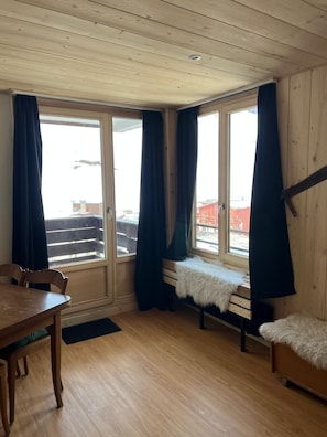 Enjoy a warm and inviting space with a dining table, sofa, and bench, offering a view of the snowy outdoor area through a large sliding glass door.