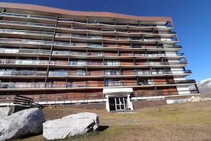 Hotel features a unique architectural design with balconies on each floor, set amidst a natural entrance area with large rocks.