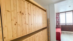 A room with a wooden wardrobe, a red bed, and a window with curtains. - 100m from resort center, 4th floor, balcony, ski locker, 18m², Tignes (Tignes)
