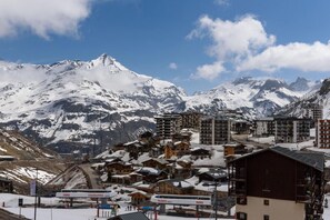 Uma cidade nas montanhas coberta de neve, com casas de madeira tradicionais e edifícios modernos, um posto de gasolina e vista desobstruída das montanhas.