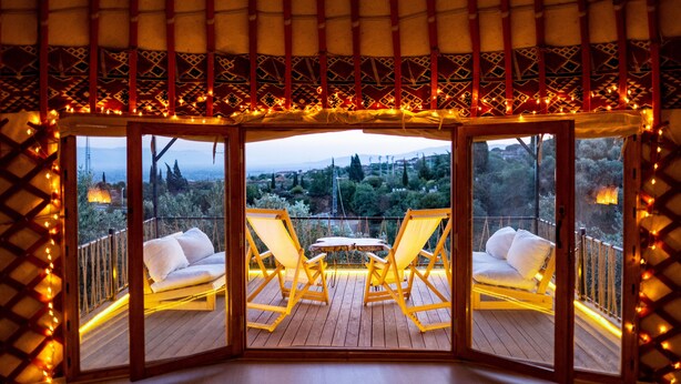 Un espacio exterior acogedor con dos sillas amarillas y una mesa, rodeado por una terraza de madera y un techo con diseño.
