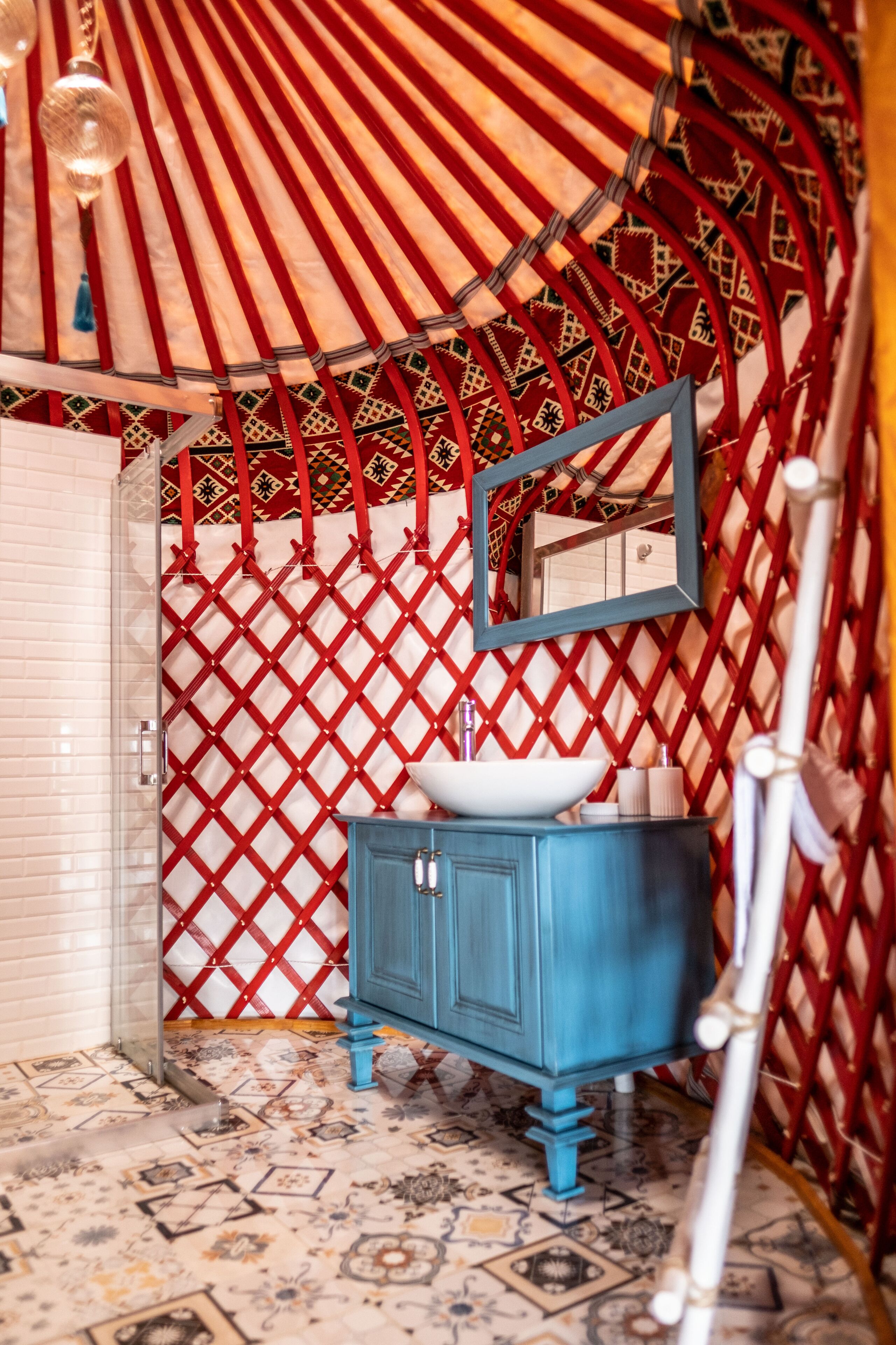 Un baño con tocador azul, lavamanos blanco y pared con celosía roja.