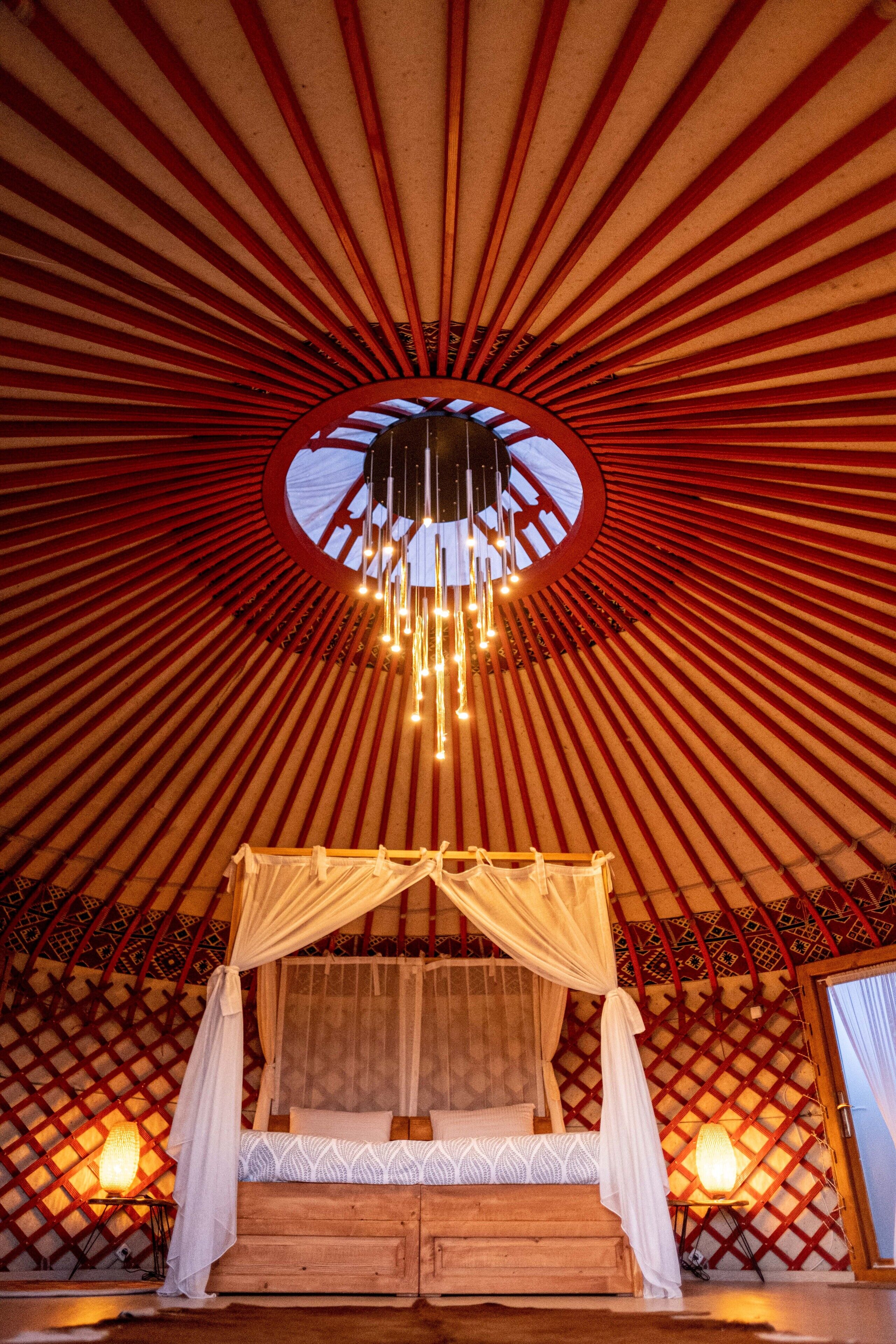 Et traditionelt yurt-soveværelse med seng, baldakin og hængende lys.