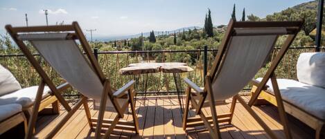 A wooden deck with two wooden chairs and a small table, overlooking a scenic landscape with trees and hills.