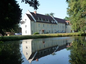 A large, multi-story building with a symmetrical facade, a central staircase, and a calm water body in front reflecting the building. - Ferienzimmer Nr. 33 - Schullandheim Reichwalde (Boxberg/Oberlausitz)