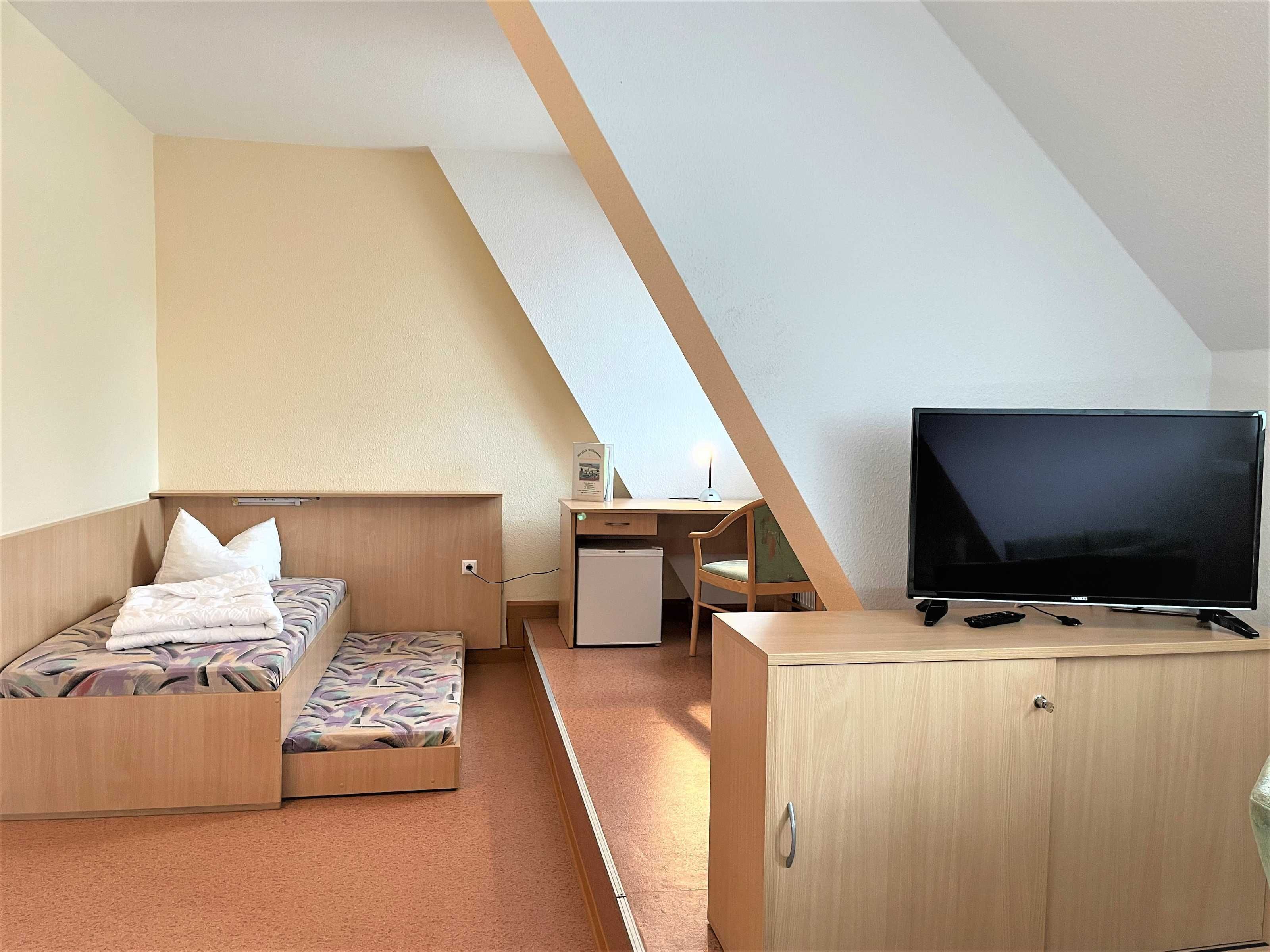 Ein gemütlicher Raum mit Bett, Schreibtisch, Fernseher und Schrank.